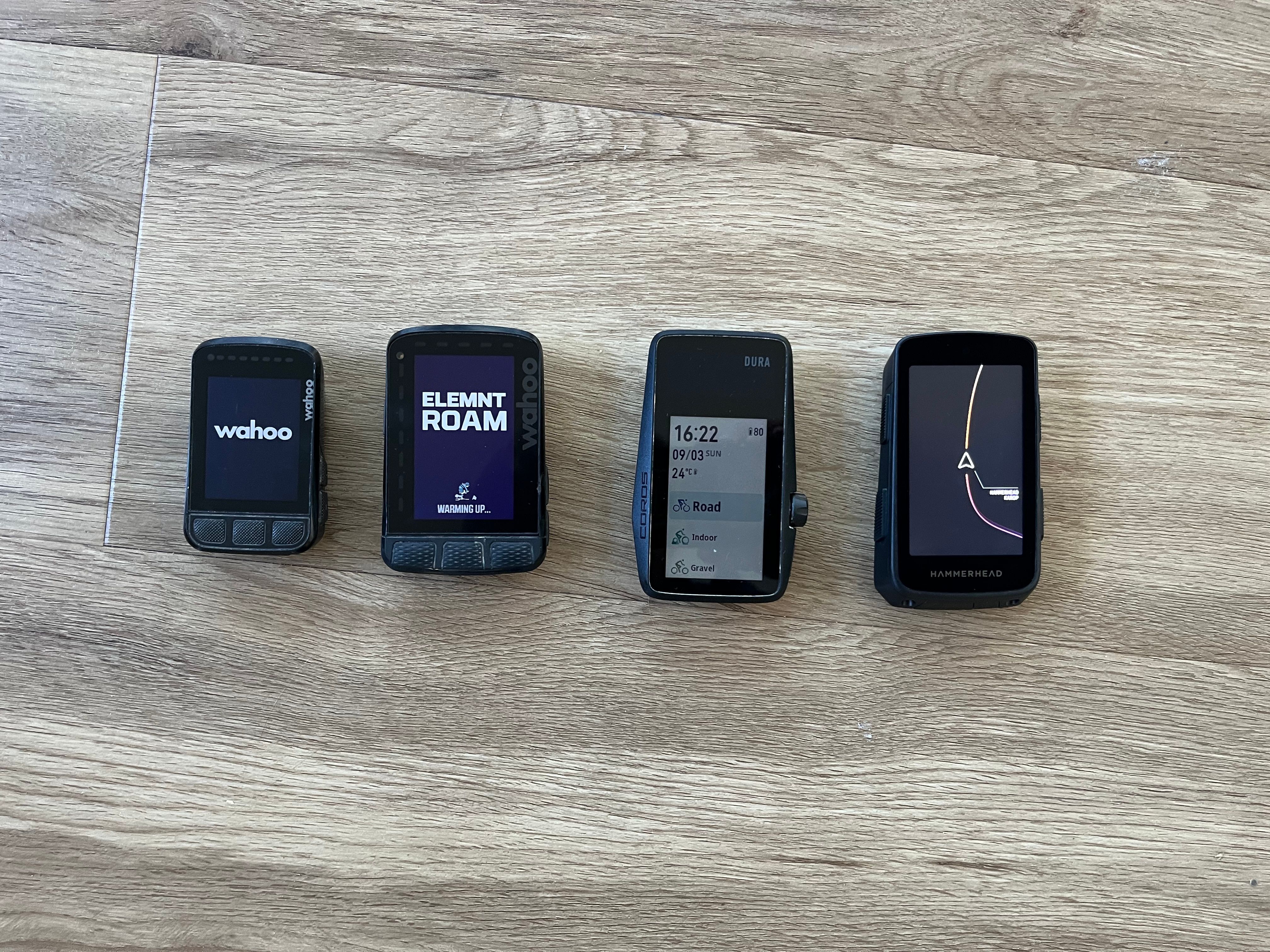 Wahoo ROAM v2, BOLT v2, Hammerhead Karoo 3 and Coros Dura next to each other. The Dura is instant ready, while the others are still booting up.