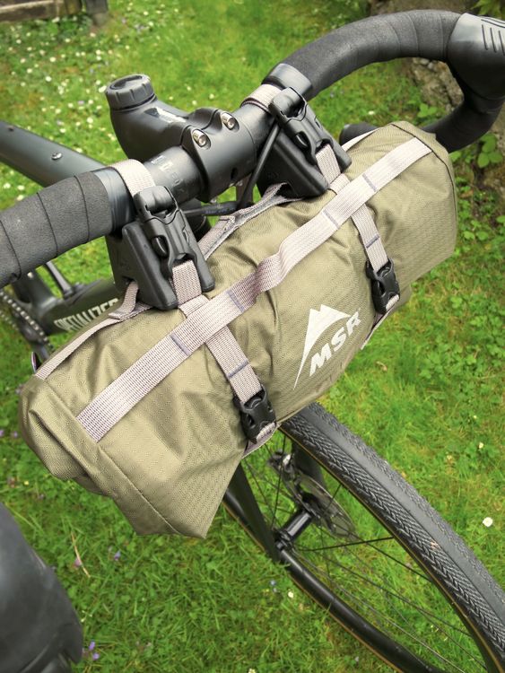 Der Packsack des MSR „Hubba Hubba Bikepack 1“ hat einen Rollverschluss, mit dem sich das Zelt stark komprimieren lässt. Dank zwei Gurten kann es direkt am Lenker befestigt werden und zwei Halterungsblöcke sorgen für zusätzliche Stabilität. 