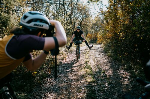 A photographer taking photos of a cyclist on a forest gravel road.